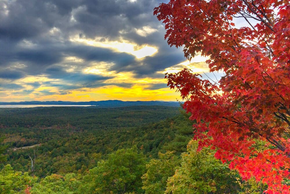 A vibrant sunset illuminates a lush, green valley framed by autumn foliage in shades of red.