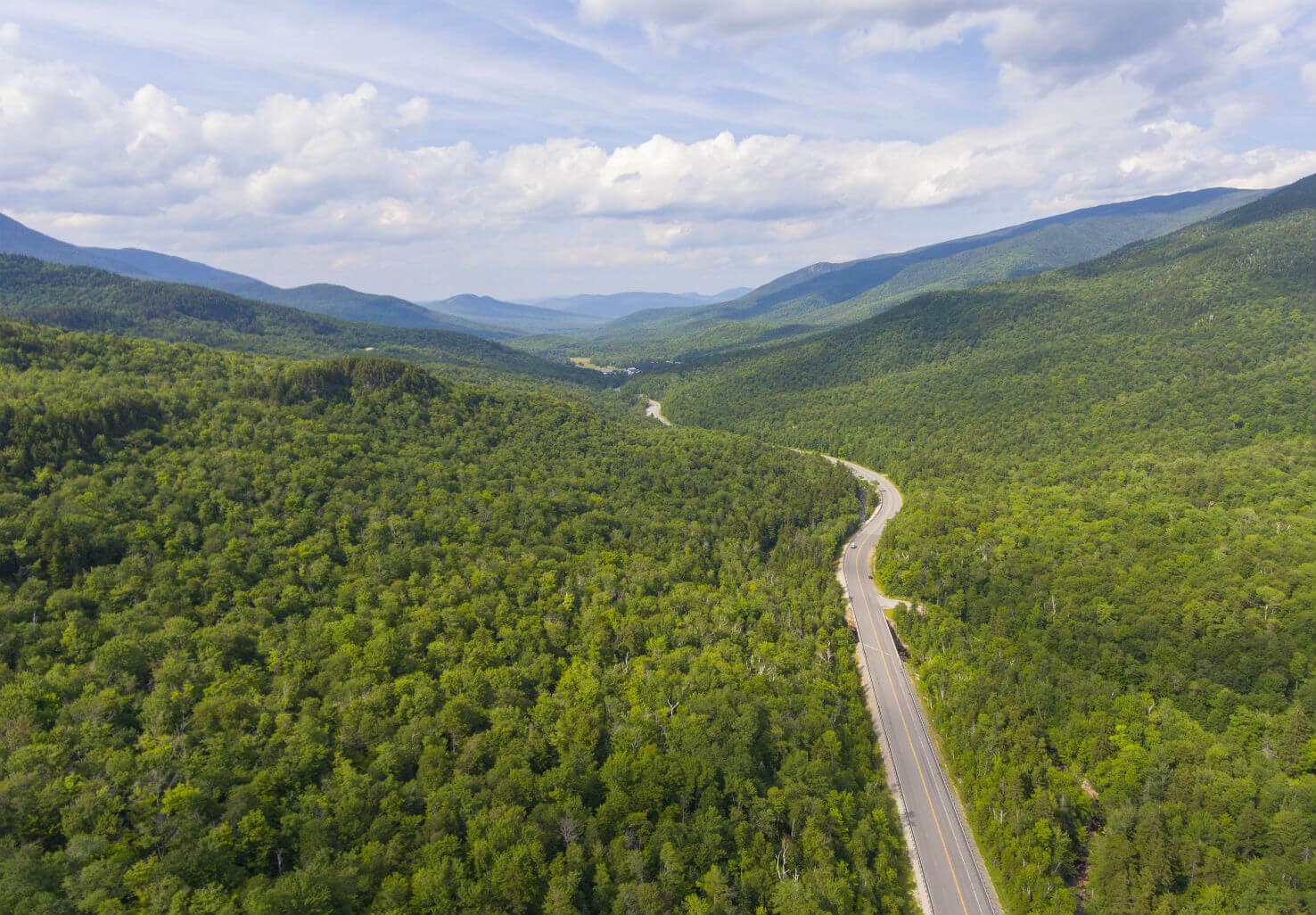 A winding road cuts through lush green mountains under a partly cloudy sky.