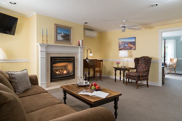 The sitting room with fireplace, sofa, coffee table, desk and wing chair.