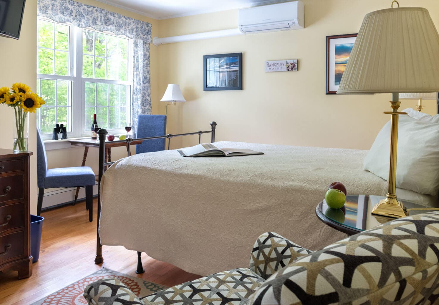 Bedroom showing the queen bed, parsons chairs, small table, flat screen TV and dresser.