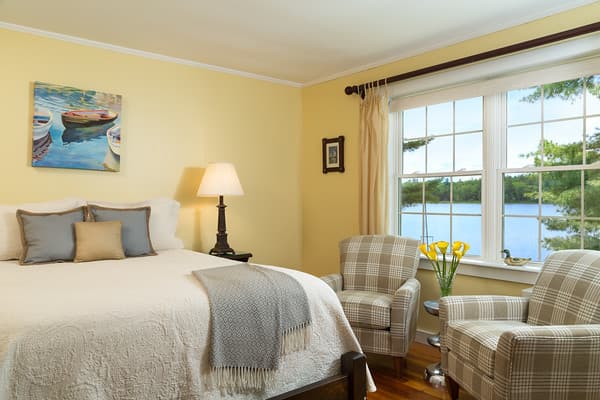 Bedroom showing the queen bed and two comfortable chairs set by a large window overlooking Tripp Lake.