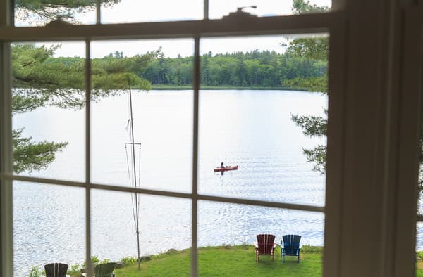 A view from the bedroom window showing adirondack chairs overlooking the lake and a kayaker.