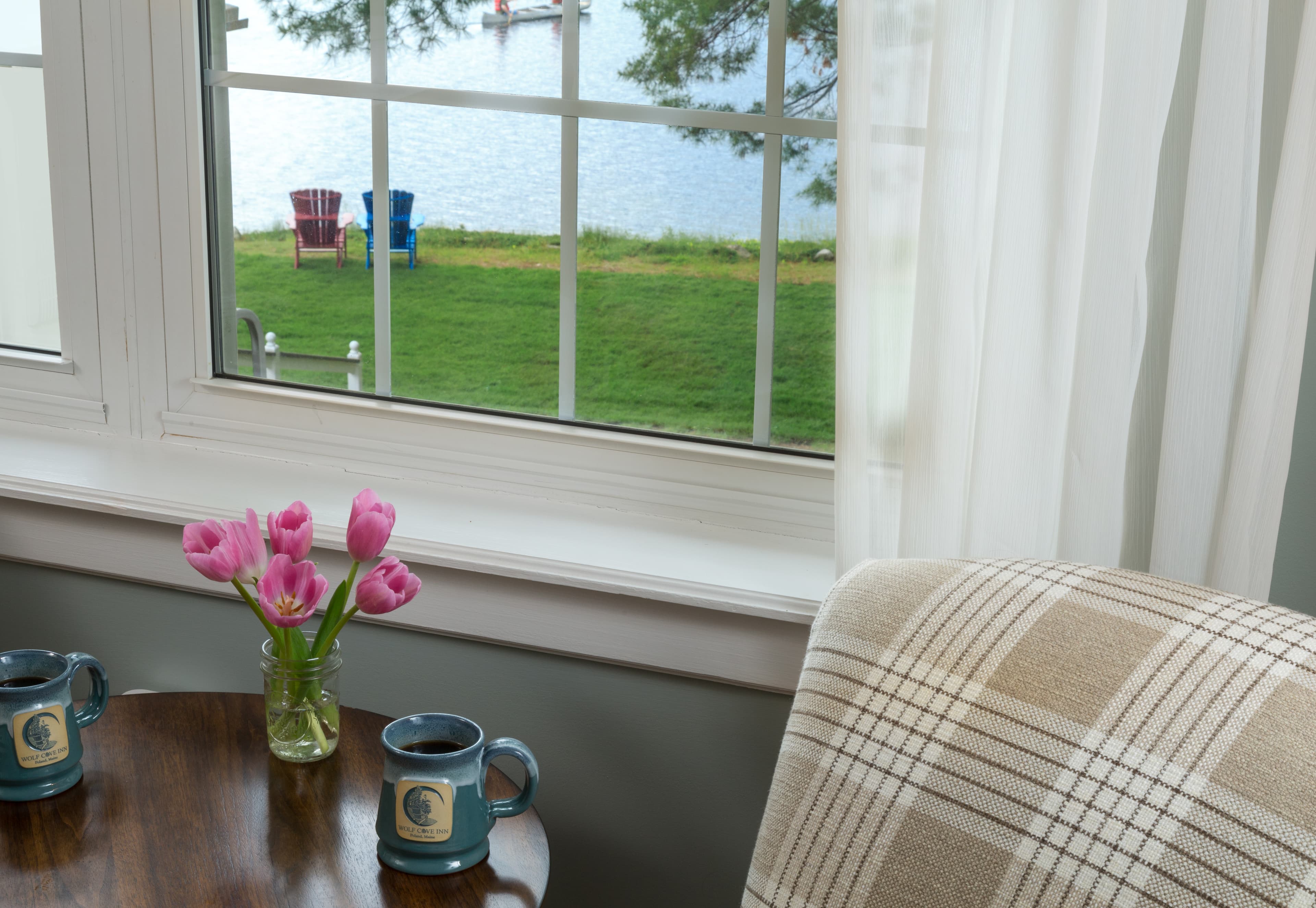 A closeup of the large window overlooking Tripp lake and adirondack chairs by the lake.