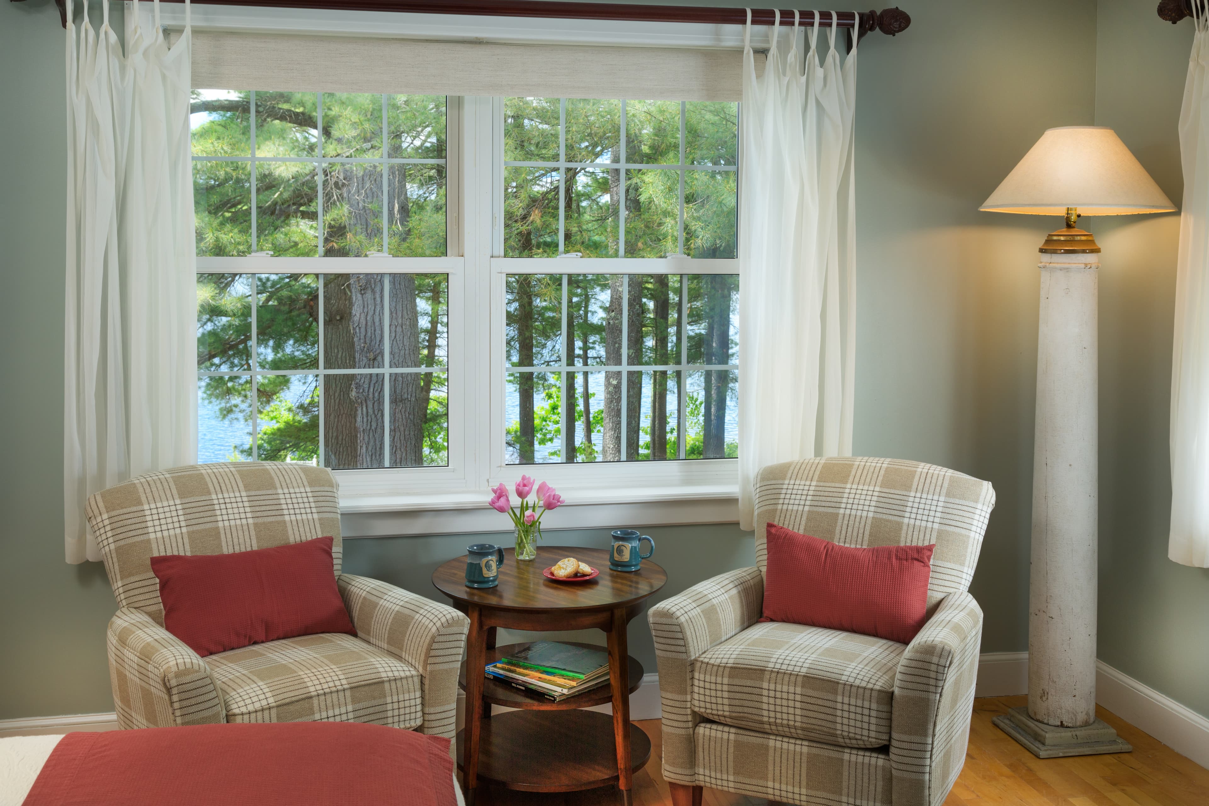 Two comfortable chairs and a small table set by a large window overlooking the pine grove and the lake.