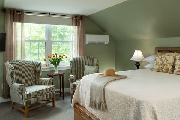 Bedroom with king bed with two wing back chairs set by the large window.