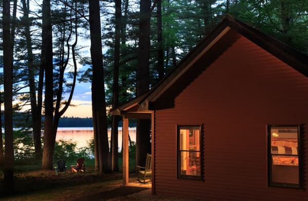 Exterior view of the cabin at sunset nestled into the pine grove overlooking Tripp Lake.
