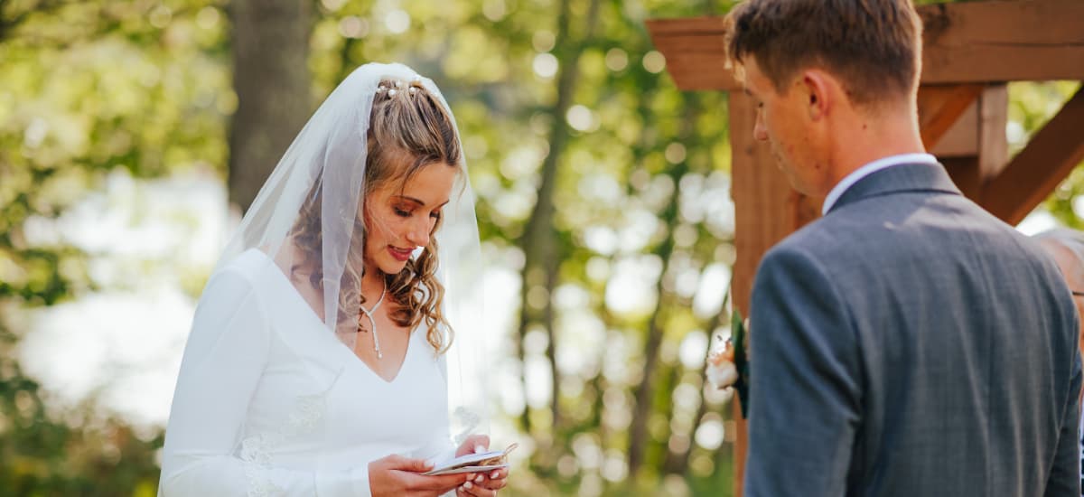 A bride reading vows to her groom during an outdoor wedding ceremony.