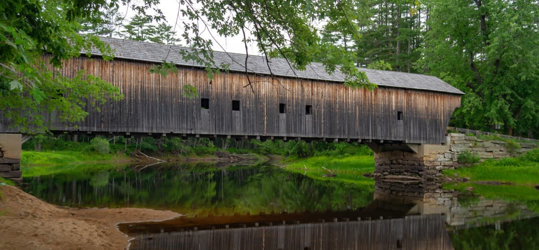 A covered wooden bridge spans a serene river surrounded by lush greenery. A covered wooden bridge spans a serene river surrounded by lush greenery.