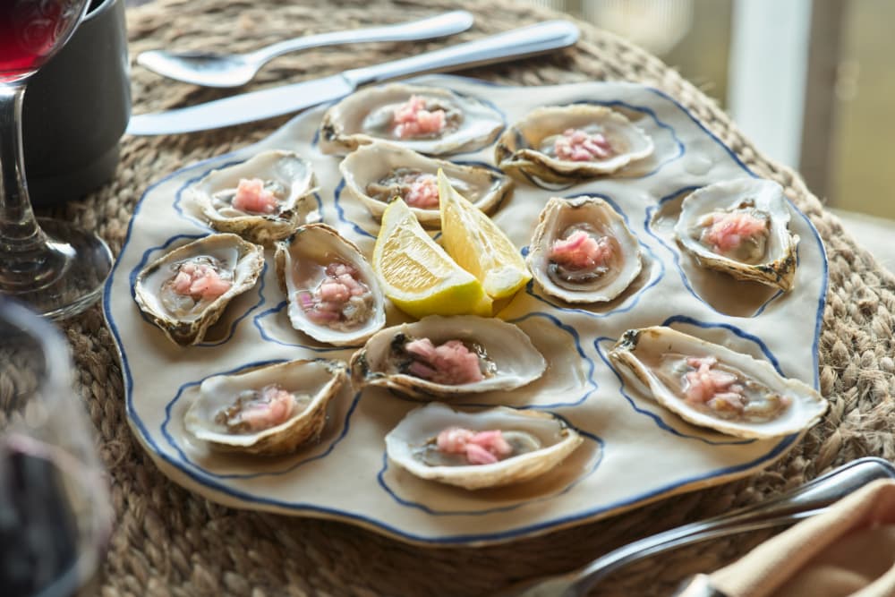 A platter of fresh oysters topped with pink sauce and accompanied by lemon wedges.