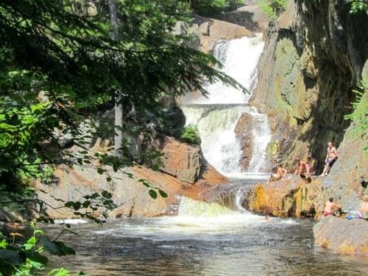 A serene waterfall cascading into a tranquil pool, surrounded by lush greenery and people enjoying the natural setting.