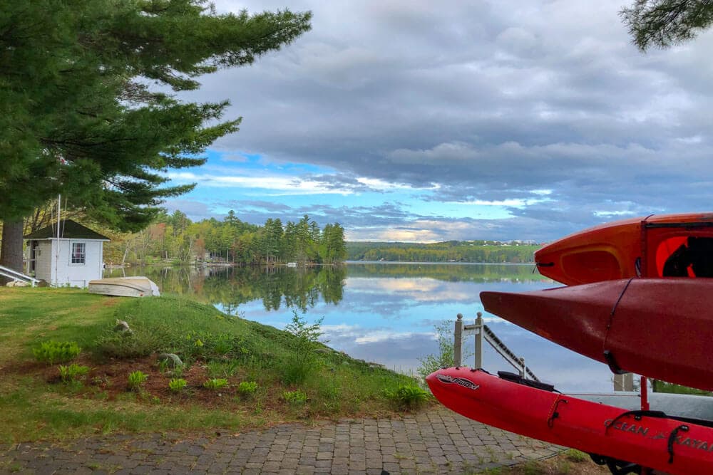 A serene lake scene with red kayaks by the shore under a partly cloudy sky.