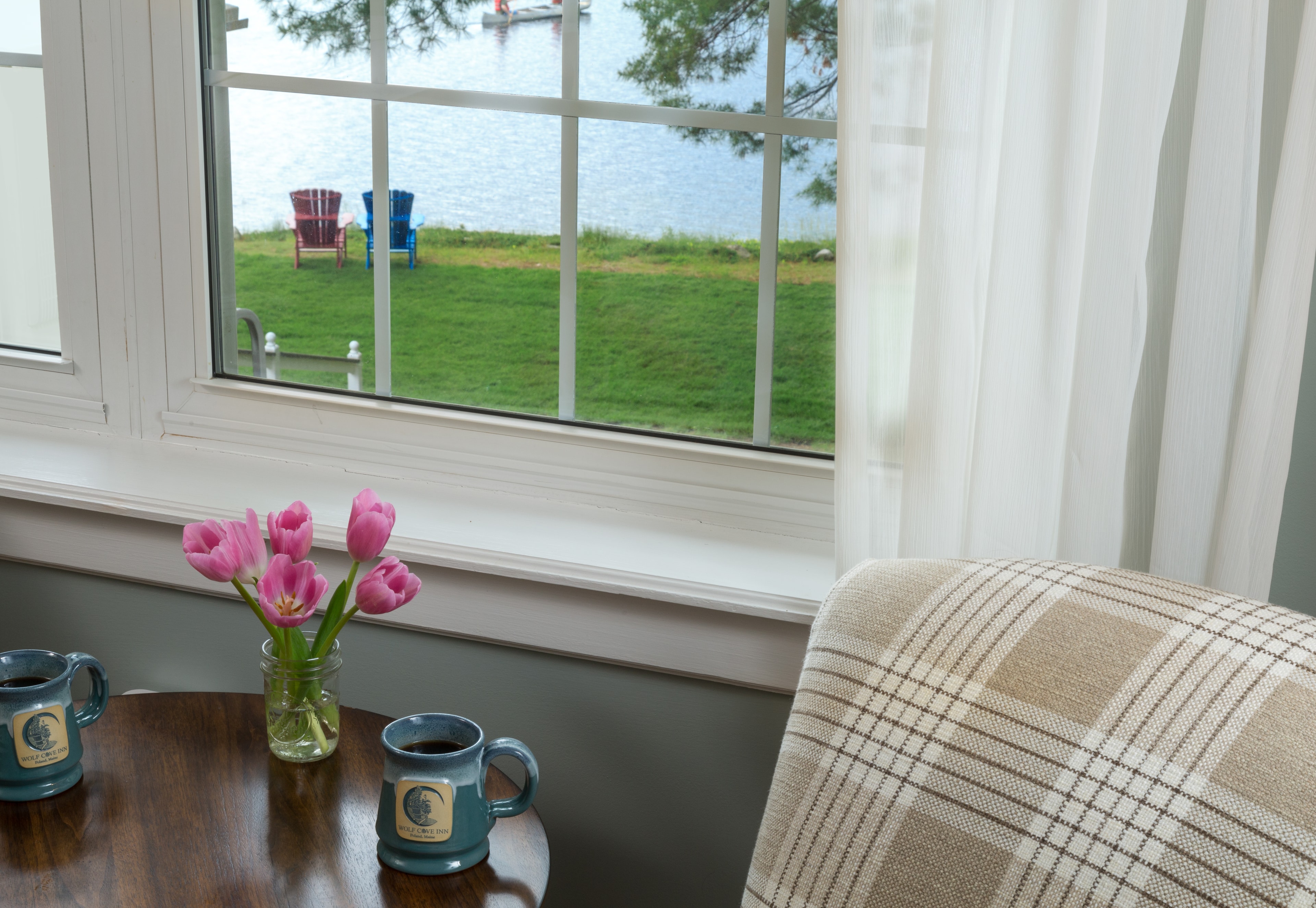 A closeup of the large window overlooking Tripp lake and adirondack chairs by the lake.