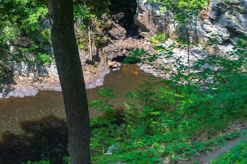 A serene forest scene with a dark, reflective body of water surrounded by rocky cliffs and lush greenery.