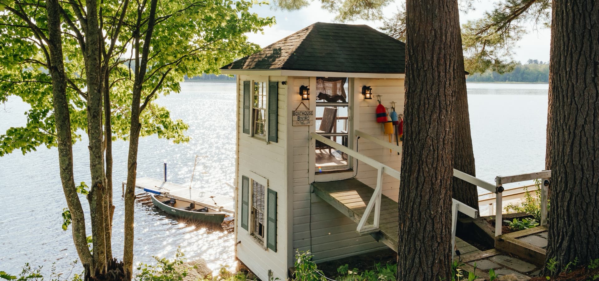 A charming lakeside boathouse with a wooden deck and greenery surrounding it.