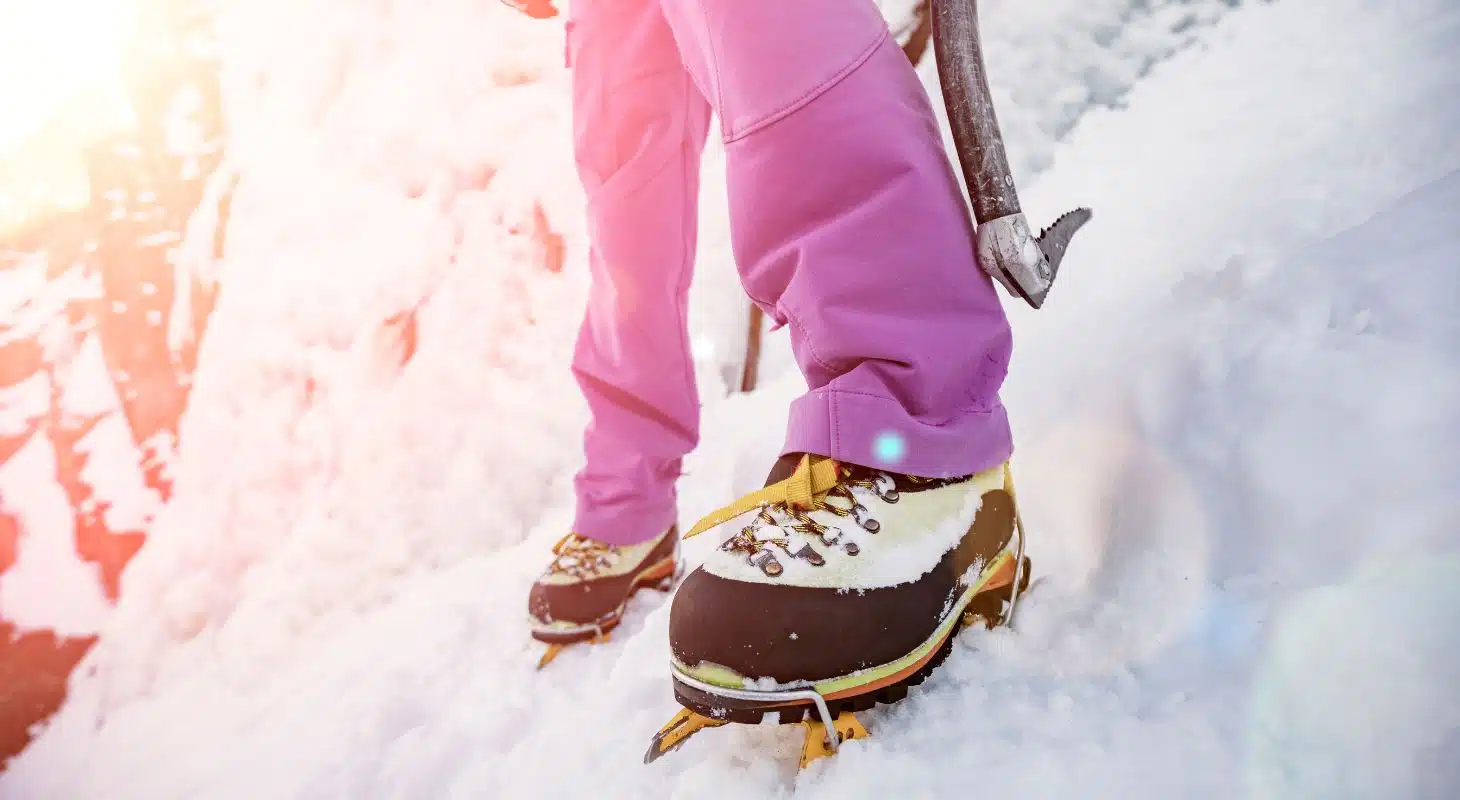 Mountaineer standing on snowy terrain with specialized boots and an ice axe.