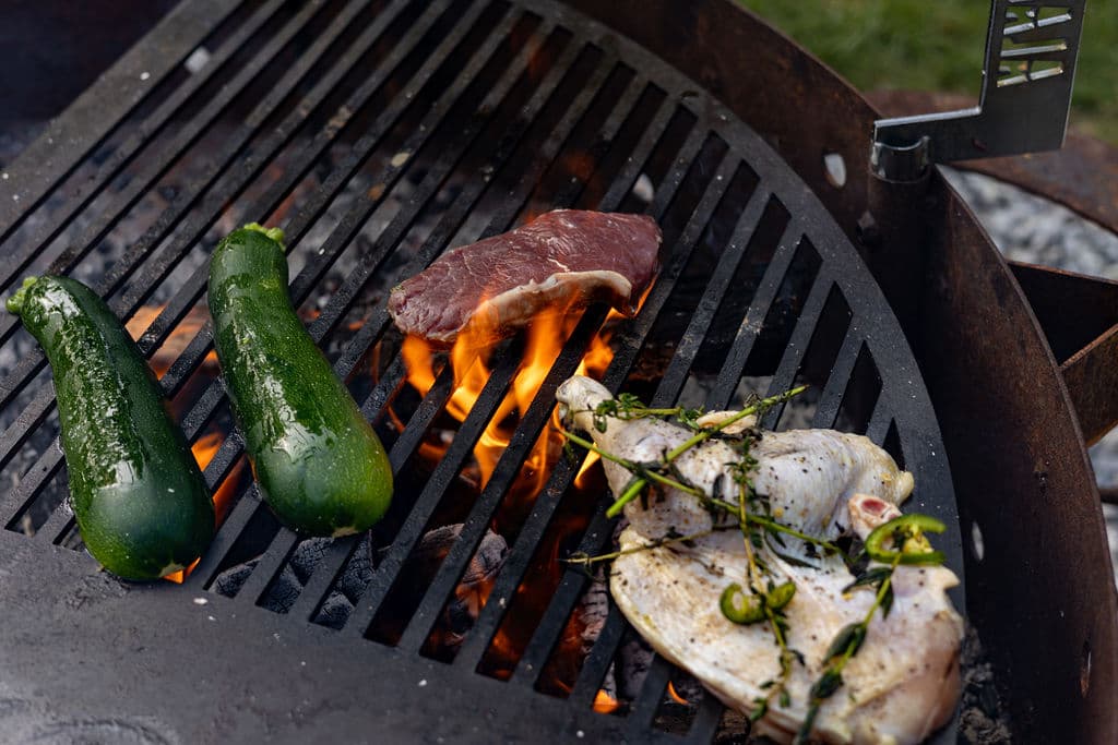 Grilled zucchini, steak, and chicken sizzling over an open flame.