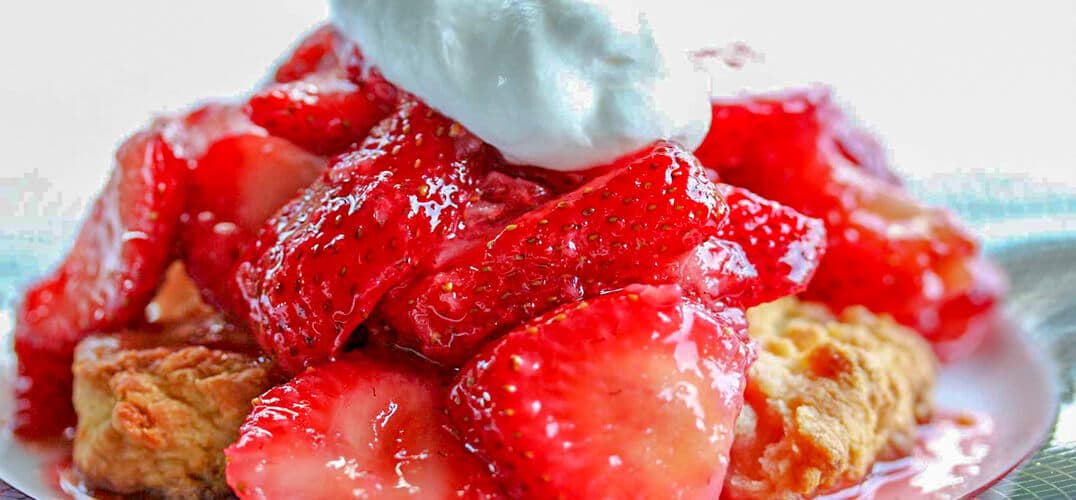 A plate of sliced strawberries topped with whipped cream and served over a biscuit. A plate of sliced strawberries topped with whipped cream and served over a biscuit.