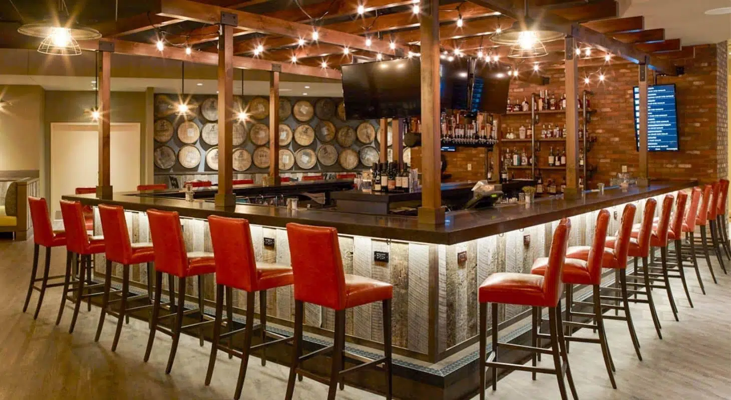A stylish bar with high red stools, a wooden counter, and an array of bottles against a brick wall. A stylish bar with high red stools, a wooden counter, and an array of bottles against a brick wall.
