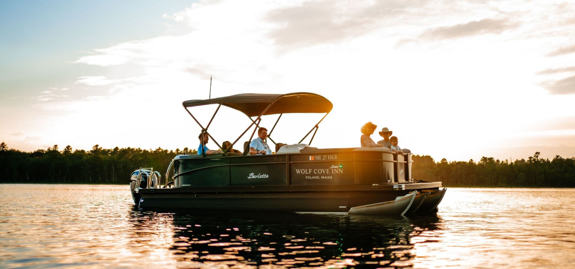 A group of people relaxes on a pontoon boat at sunset on a calm lake.