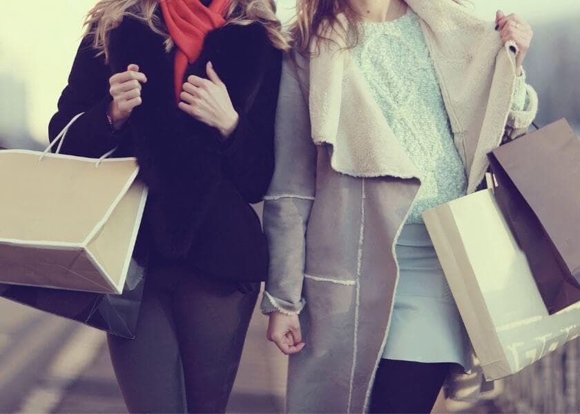 Two women walking together, holding shopping bags and each other's hands.