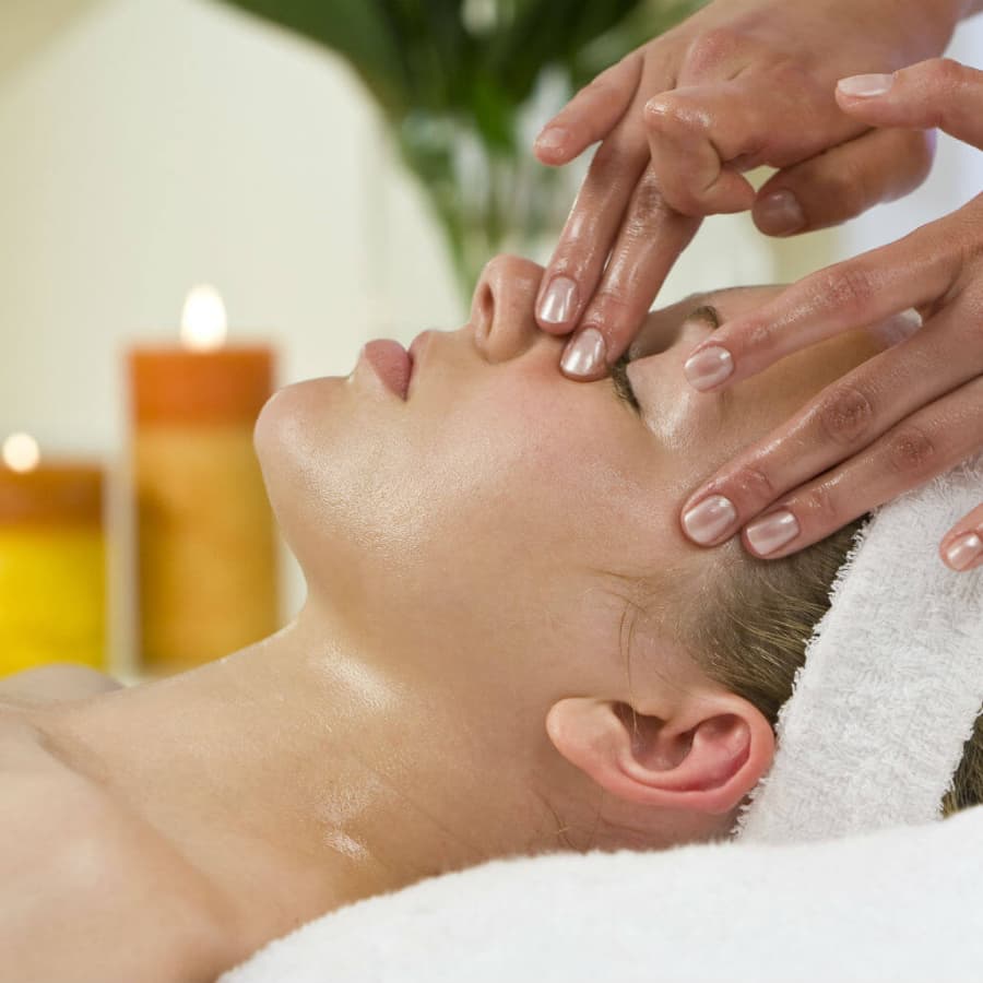 A person receiving a facial massage in a tranquil spa setting with candles in the background.