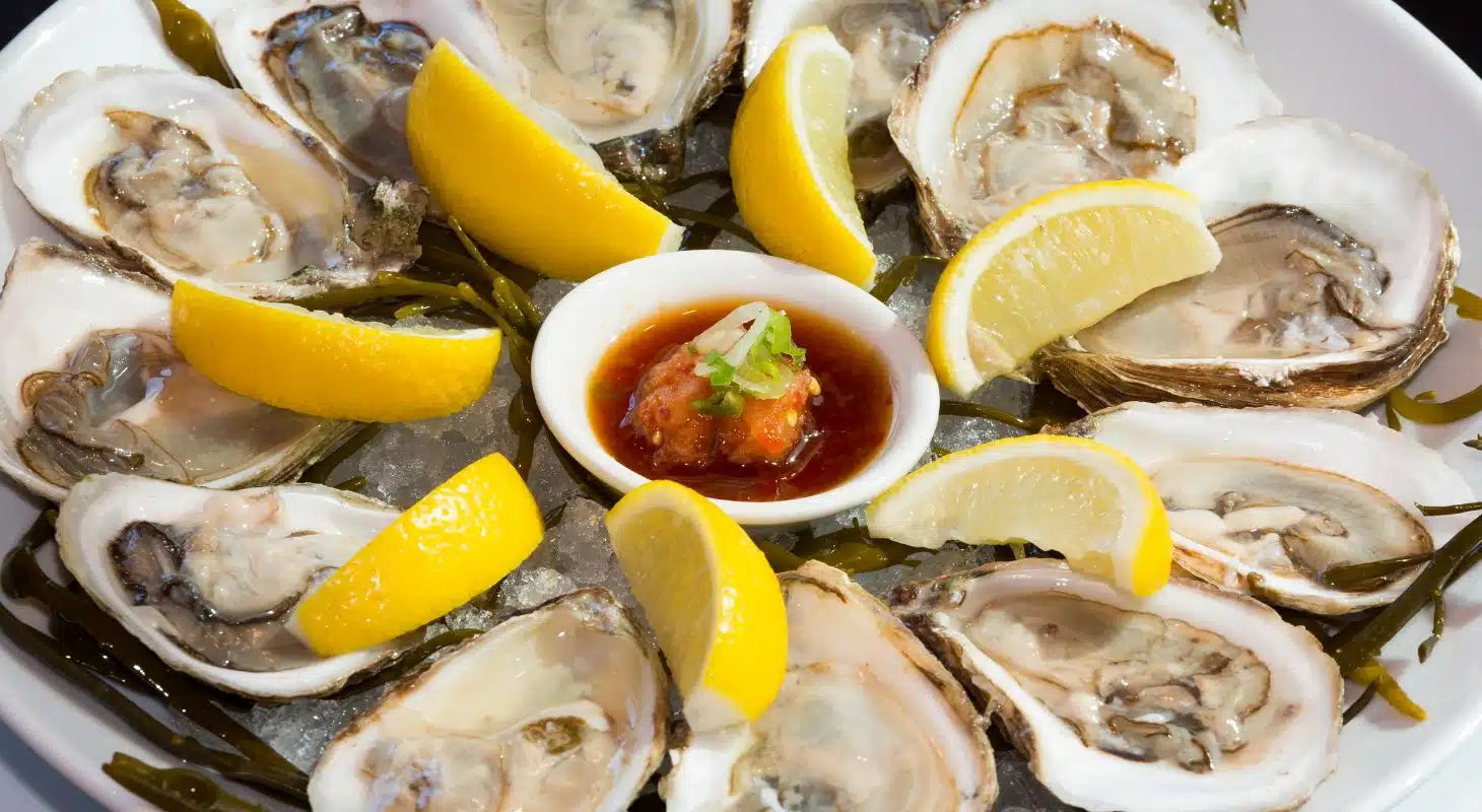 A platter of fresh oysters garnished with lemon slices and served with a dipping sauce.