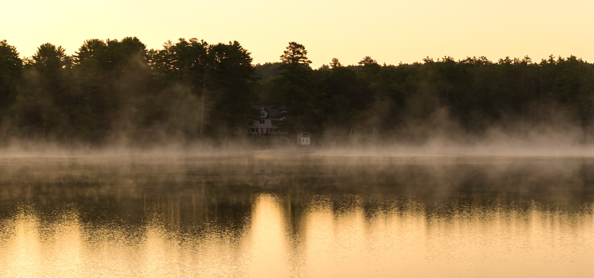 Early morning mist rises from a tranquil lake surrounded by trees.