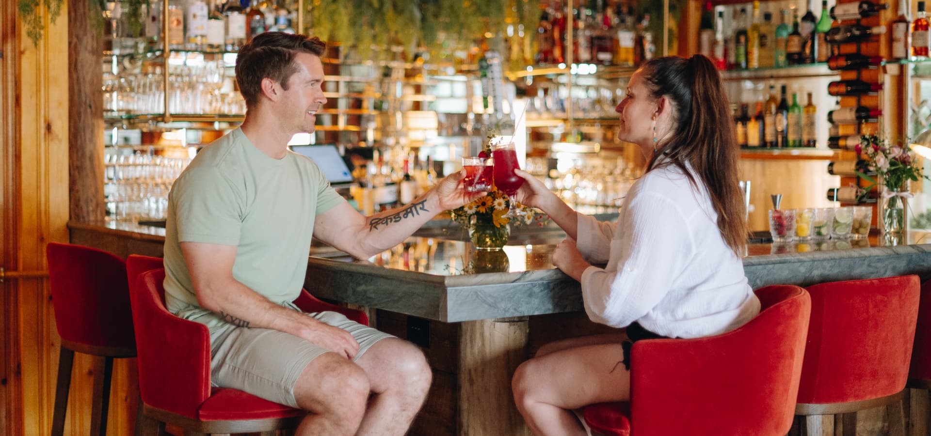 A man and a woman clink glasses while sitting at a bar.