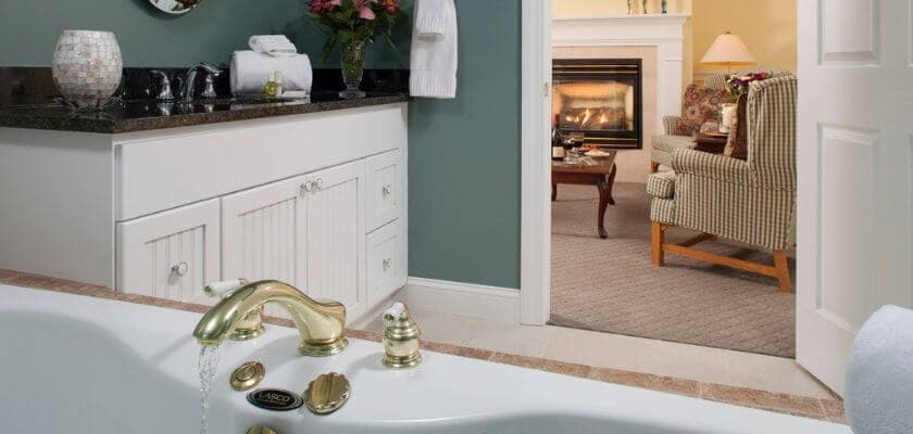 A luxurious bathroom featuring a gold faucet, a bubbling tub, and a cozy seating area with a fireplace in the background.