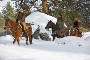 Three riders on horseback navigate through a snowy landscape.