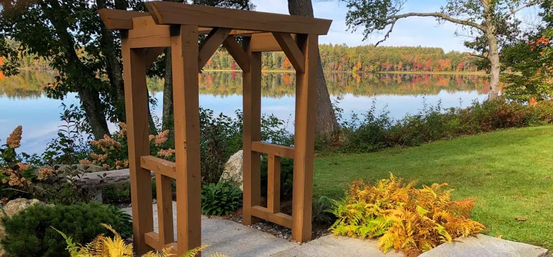 A wooden archway frames a serene lake surrounded by autumn-colored trees and lush greenery. A wooden archway frames a serene lake surrounded by autumn-colored trees and lush greenery.