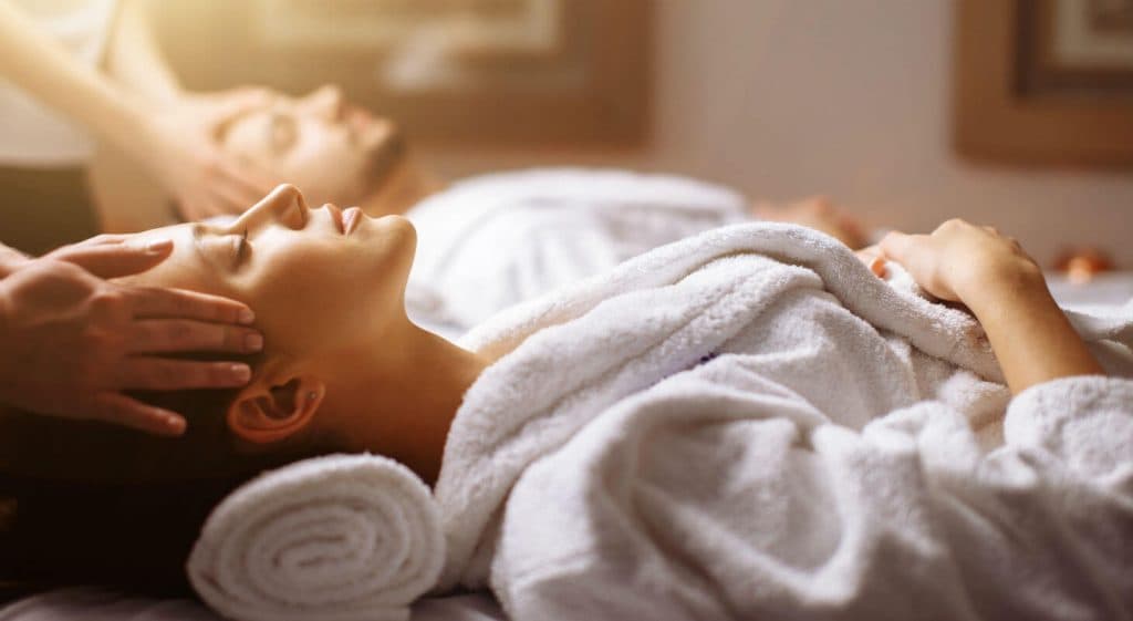 A woman receives a relaxing massage while lying next to a man in a spa setting.