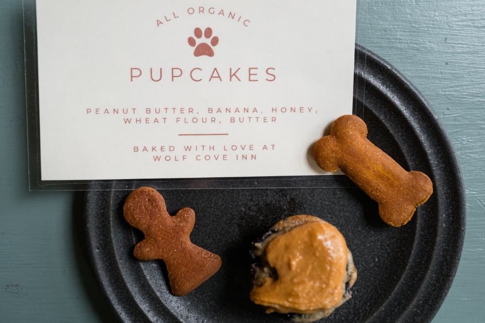 A plate with a pupcake topped with peanut butter and two bone-shaped dog treats, accompanied by a sign listing their organic ingredients.