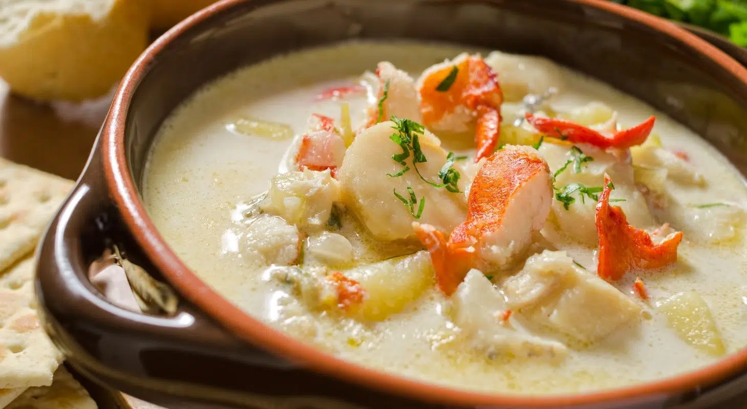 A creamy lobster chowder garnished with herbs in a rustic bowl, accompanied by bread.