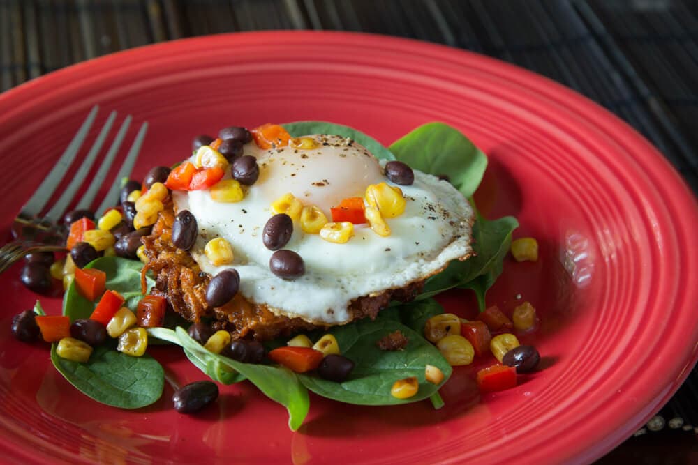 A fried egg atop a bed of spinach and colorful vegetables, served on a red plate.