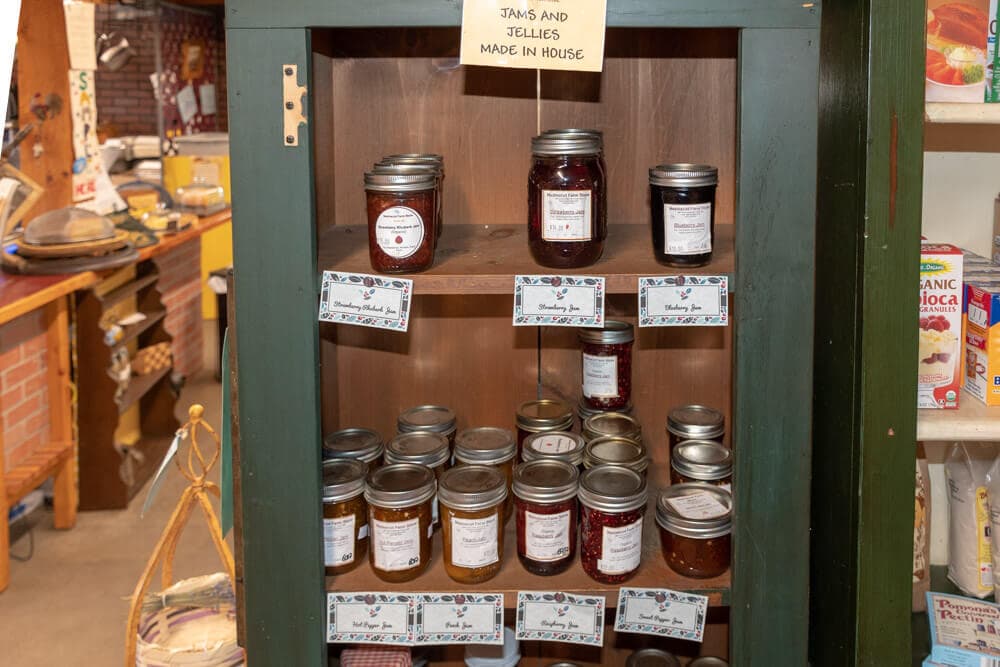 A wooden shelf displaying various jars of homemade jams and jellies with labels.