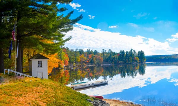A serene lakeside scene with autumn foliage and a small white building reflected in the calm water.