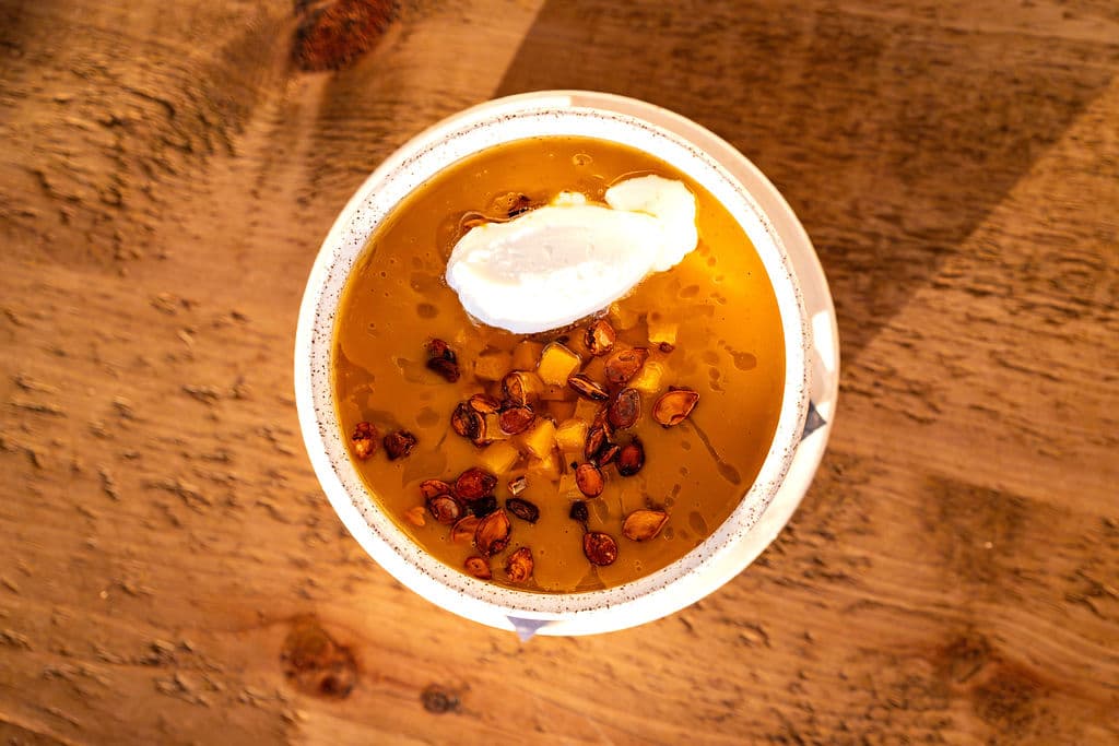 A bowl of golden soup topped with a dollop of cream and sprinkled with nuts.
