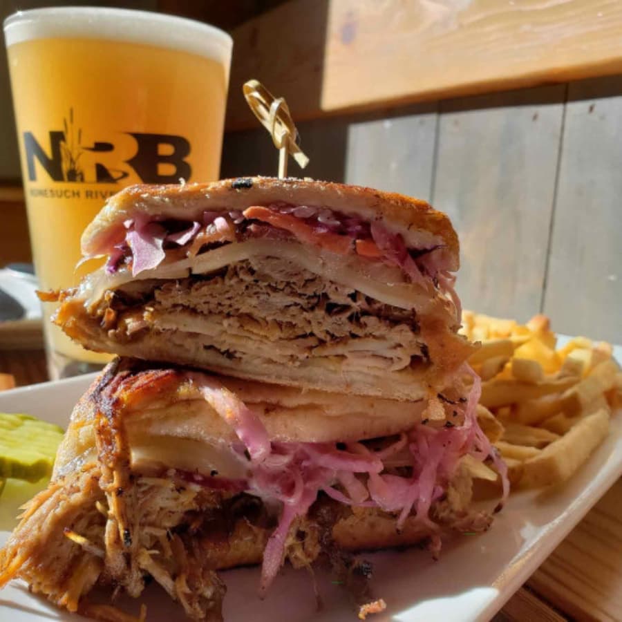 A stacked sandwich with layers of meat and toppings, served with fries and a pint of beer in the background.