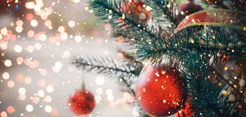 Close-up of a Christmas tree with red ornaments and sparkling lights in the background.