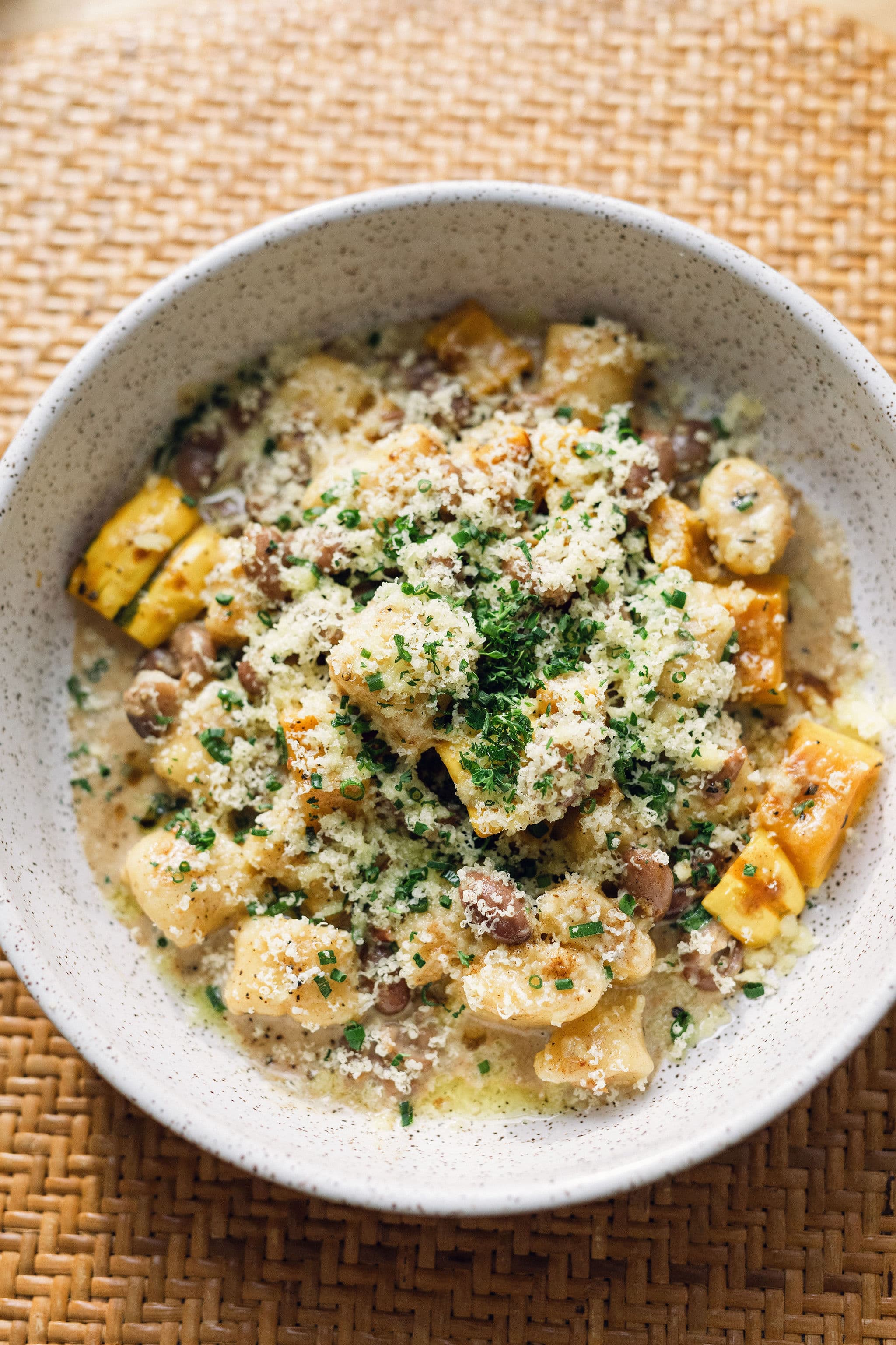 A bowl of creamy pasta topped with cheese, herbs, and diced vegetables.