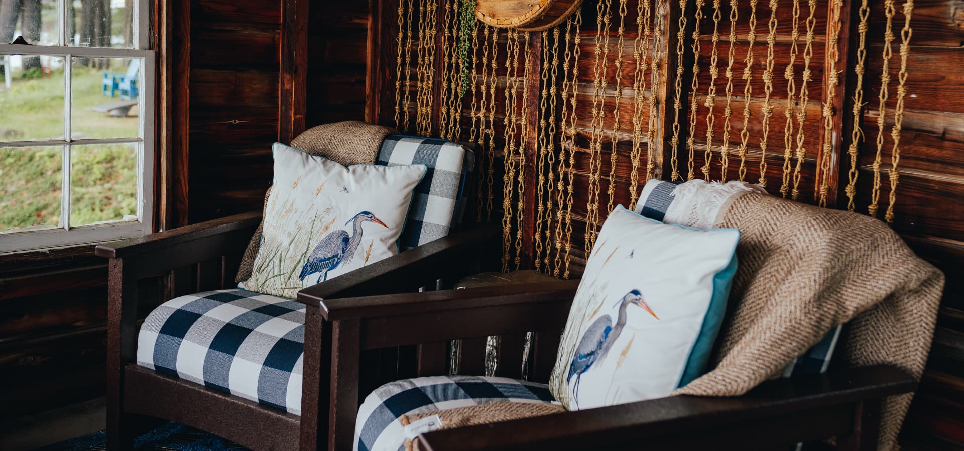Two wooden armchairs with decorative pillows featuring a heron, set against a wooden wall with hanging decor.