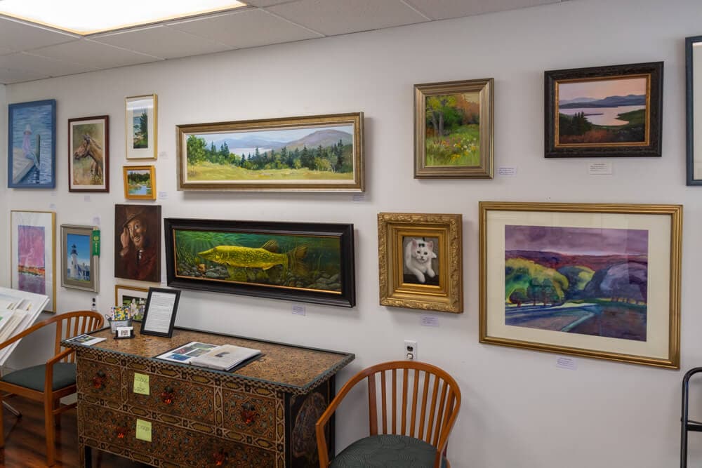 A wall adorned with various framed paintings, alongside a decorative table and two wooden chairs.