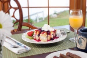 A plate of dessert topped with whipped cream and berry sauce, accompanied by a glass of orange juice and a coffee cup.