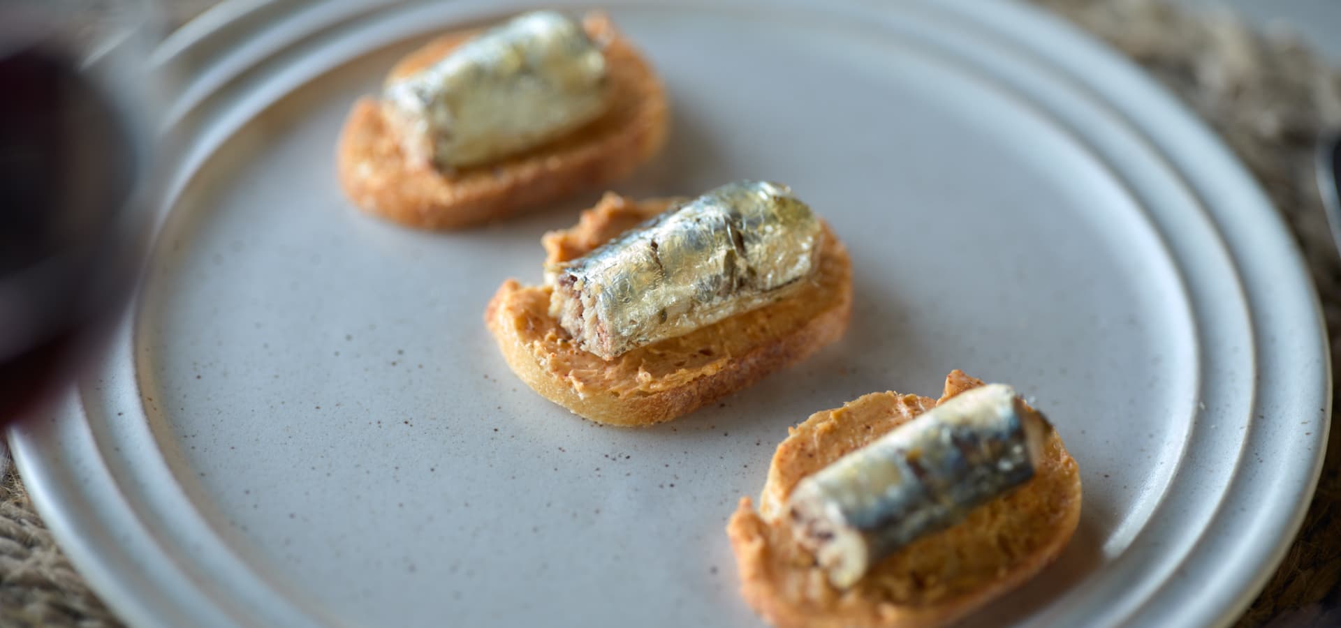 Three pieces of toasted bread topped with sardines on a light-colored plate.