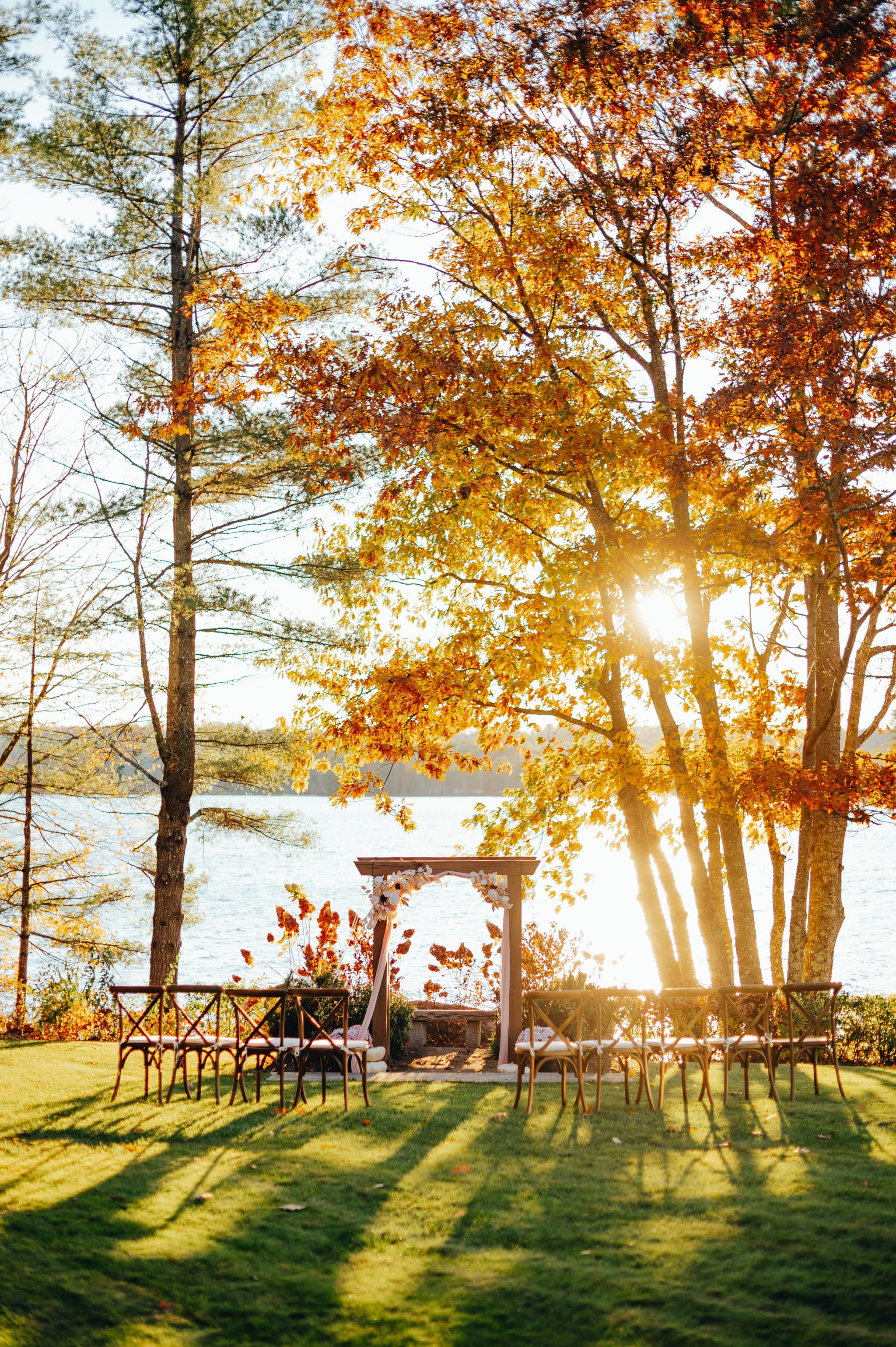A serene outdoor setting with fall foliage, a wooden archway, and empty chairs overlooking a lake.