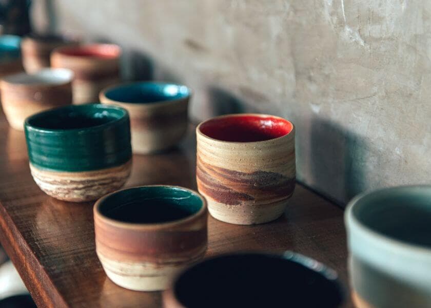 A variety of colorful ceramic cups arranged on a wooden shelf.