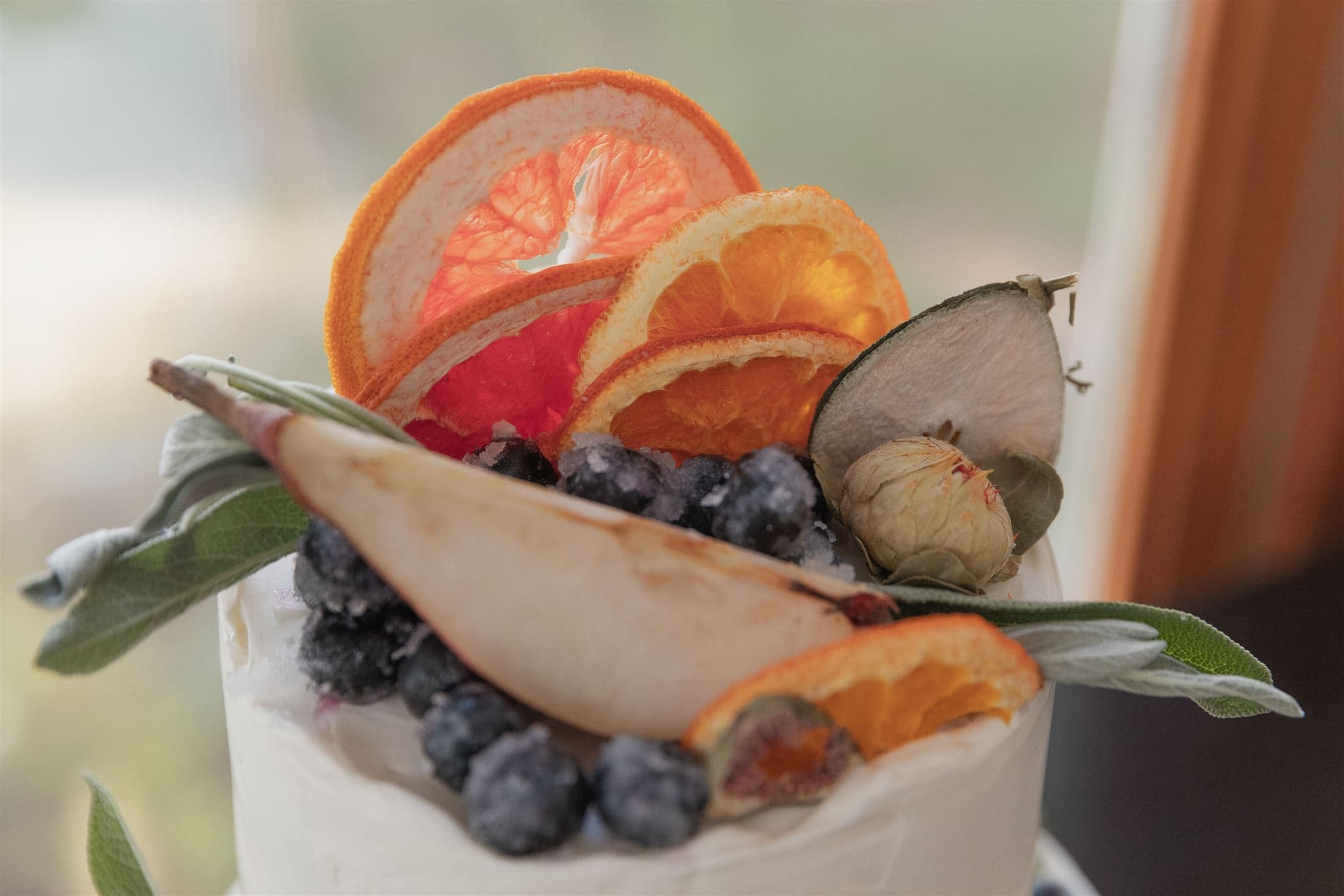 A beautifully decorated cake topped with dried citrus slices, blueberries, and decorative leaves.