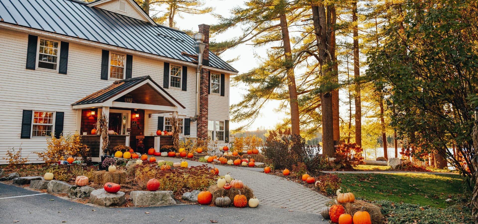 A cozy white house surrounded by colorful pumpkins and autumn foliage.