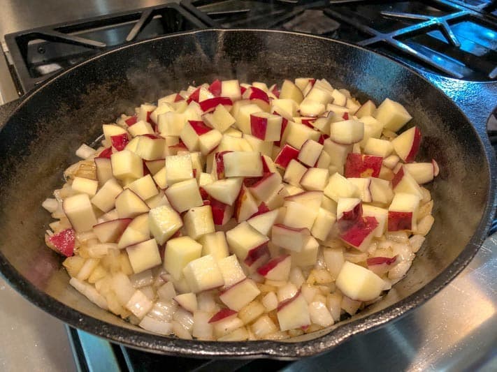 Diced red and white potatoes sautéing with onions in a cast iron skillet.